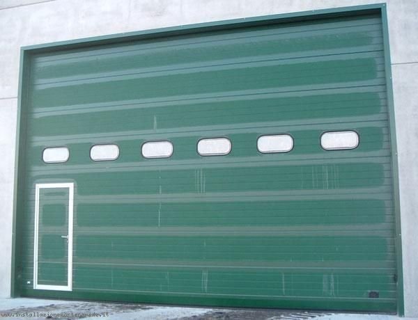 Portone sezionale industriale verde con oblò e porta pedonale a Torino
